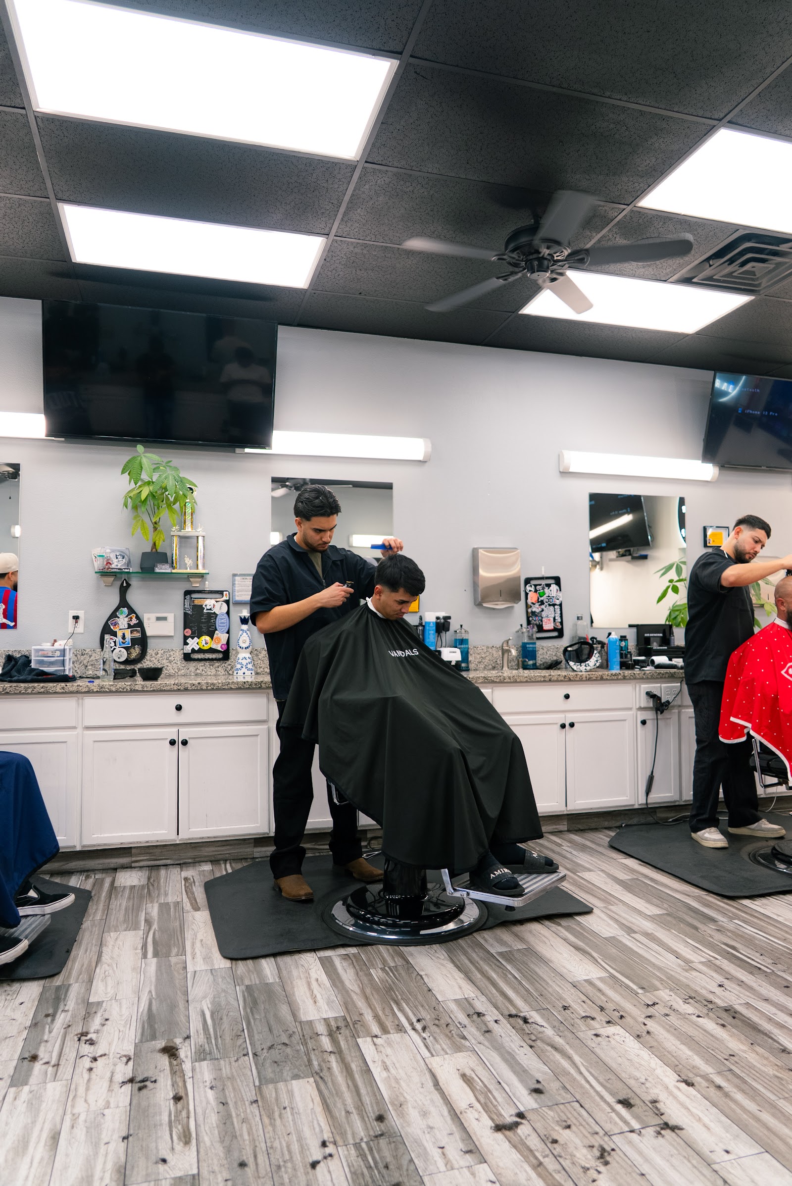 Barbers cutting clients' hair inside a bright barbershop with mirrors and TVs