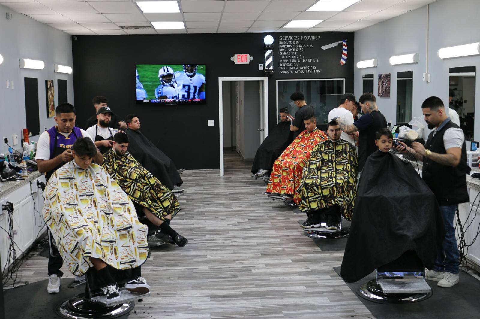 Busy barbershop with multiple barbers cutting clients under a services price board
