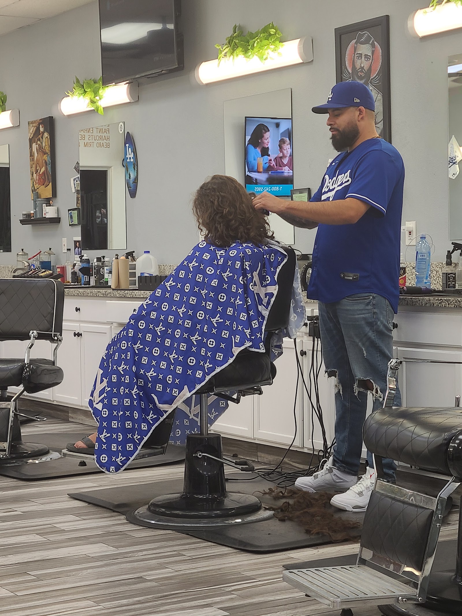 Barber in a Dodgers jersey cutting a client's curly hair