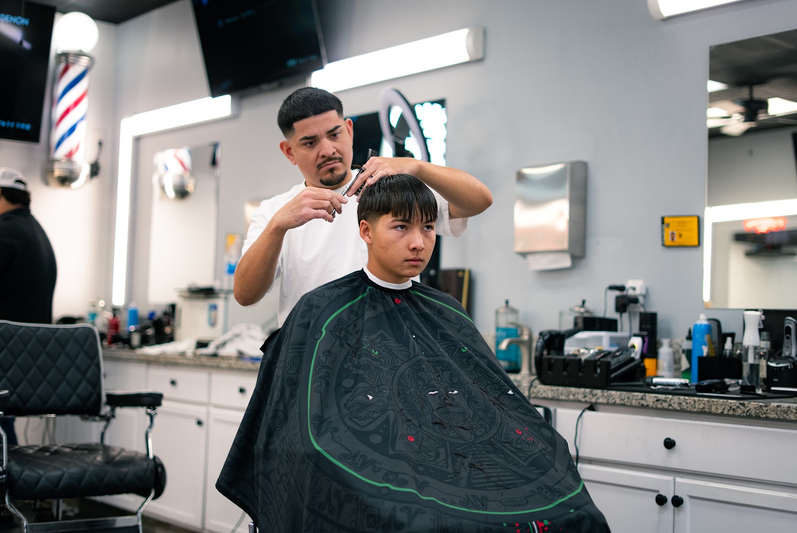 Barber trimming a young client's hair at Studio Barbershop, front view with cape on